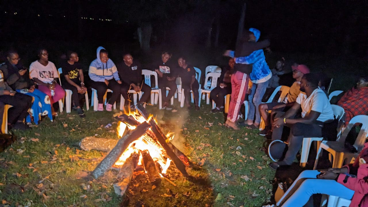 Campers seated in a circle around a bonfire at night at the FOCUS Campsite