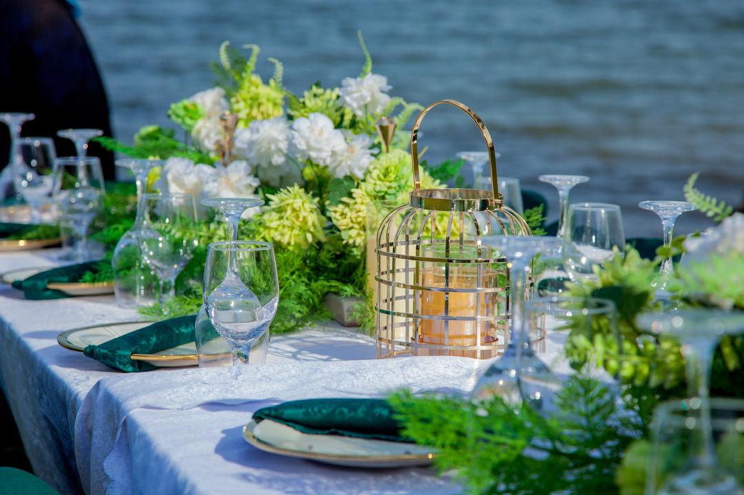 A dinner table set with flowers and lanterns at the water's edge