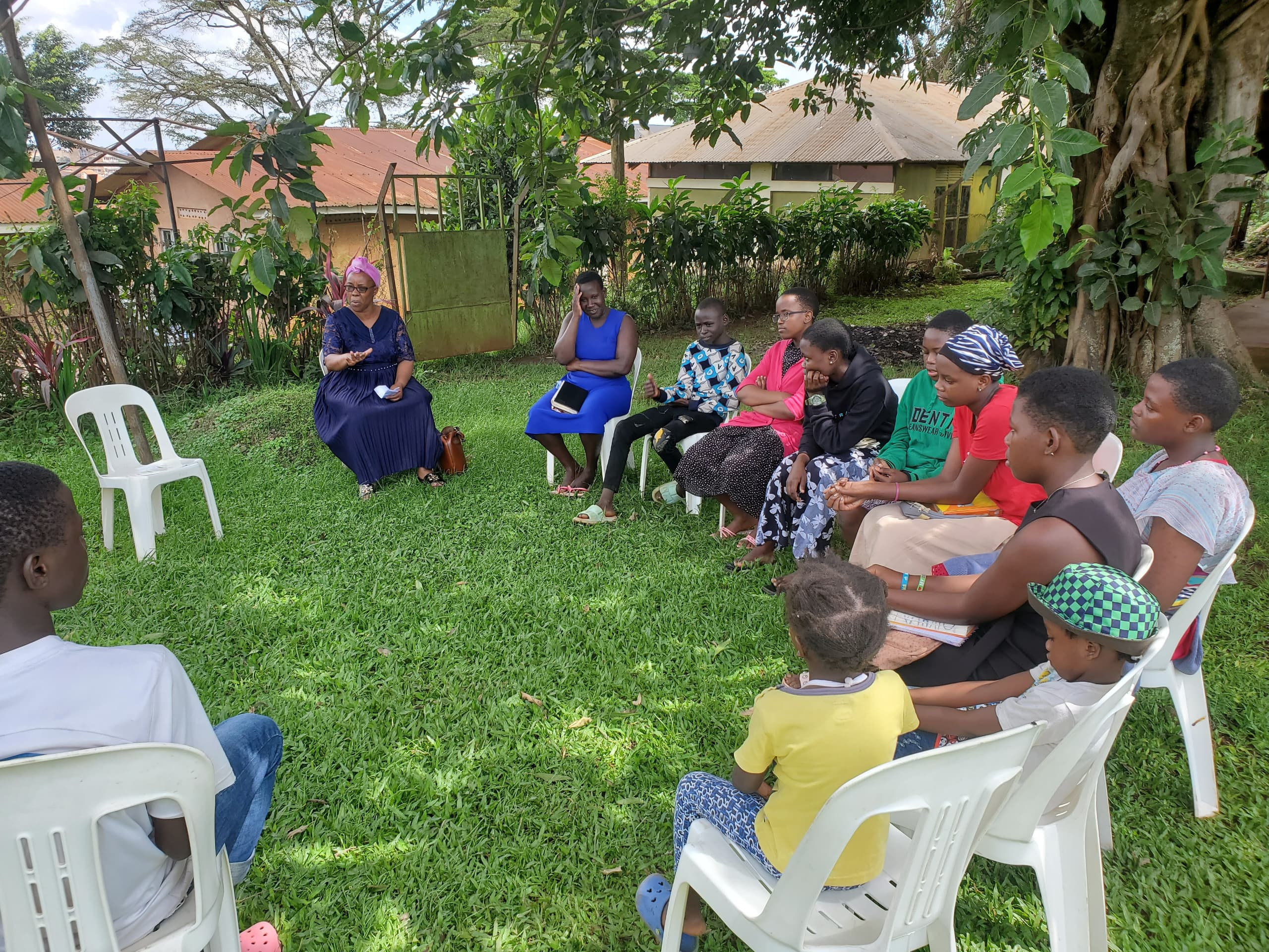 Children and teenagers seated in a circle on the lawn as two women lead a mentoring session