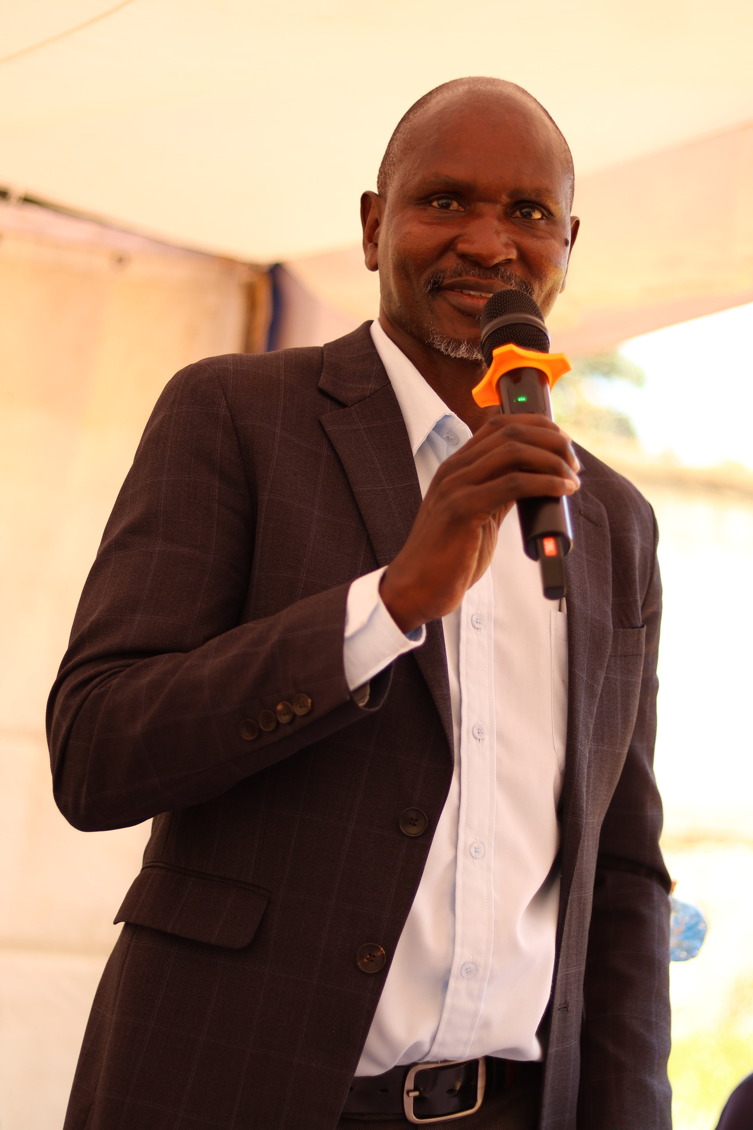 Sam Opolot, FOCUS board member, speaking into a microphone under a tent