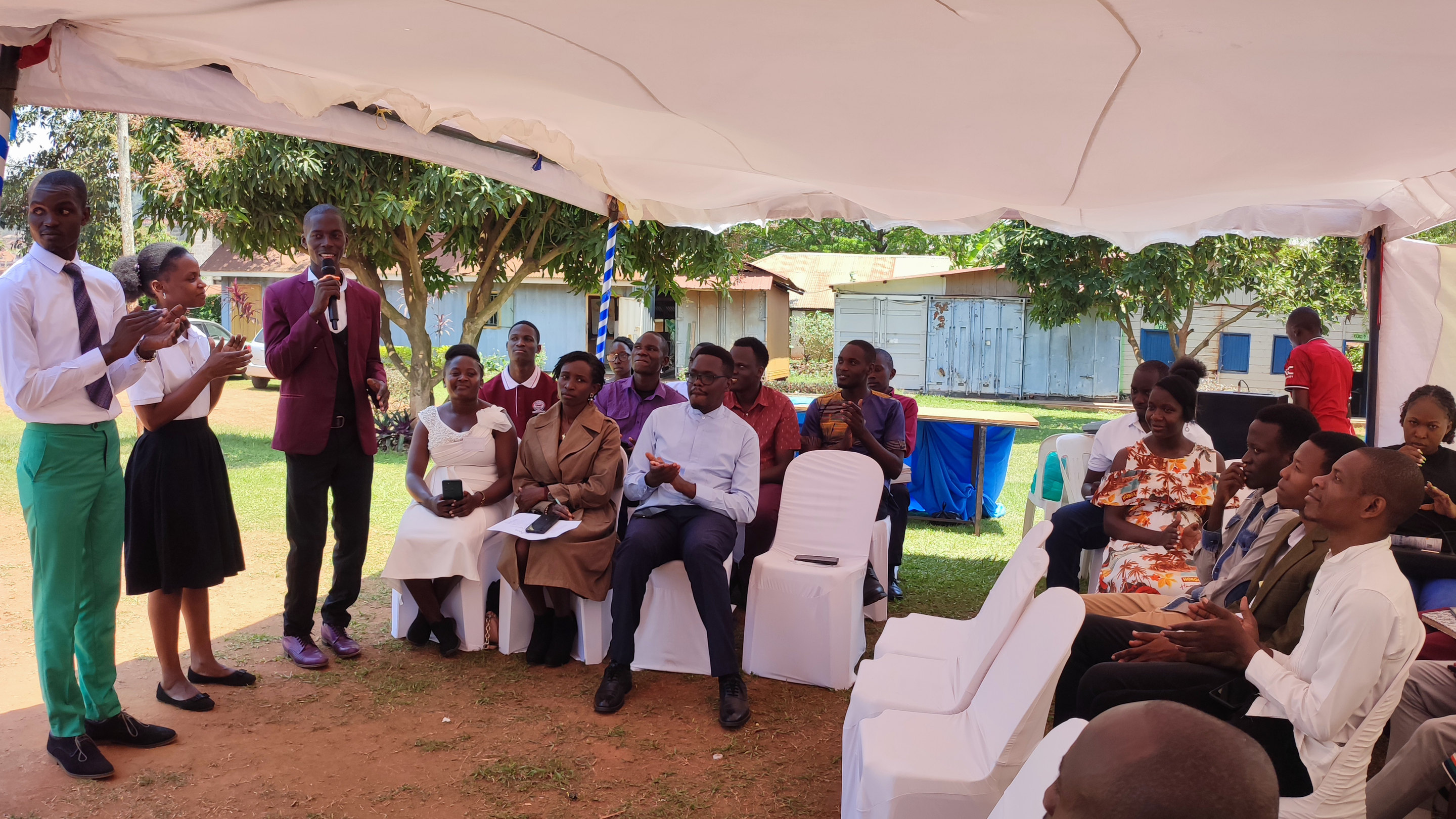 A STEM gathering under a tent, a speaker addressing students and guests seated on the grass
